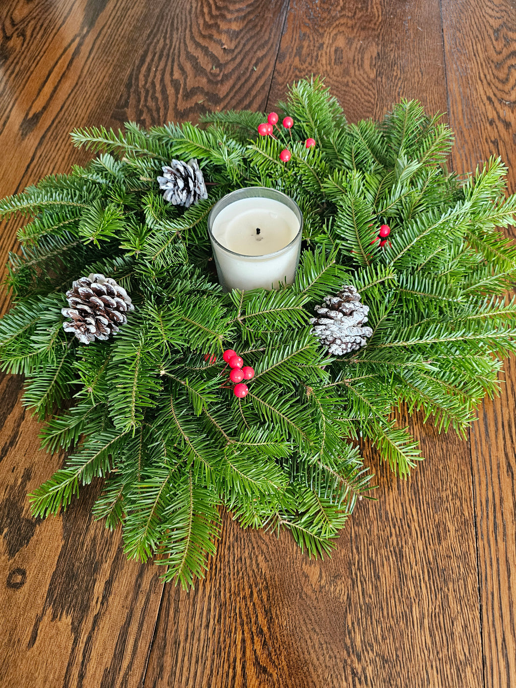 Christmas wreath with a candle, pine cones, and berries on a wooden surface
