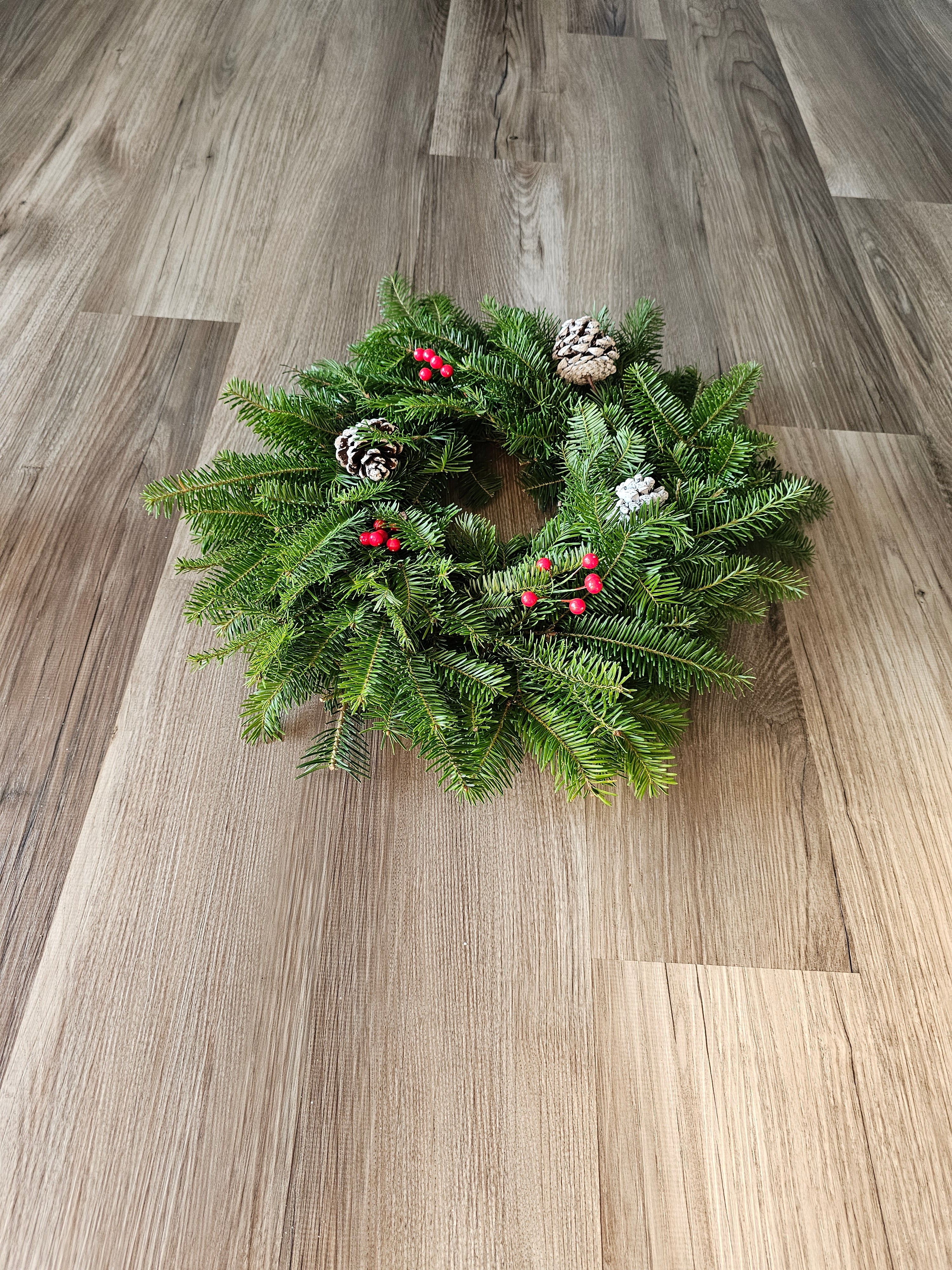 Green Christmas wreath with pinecones and berries on a wooden wall.