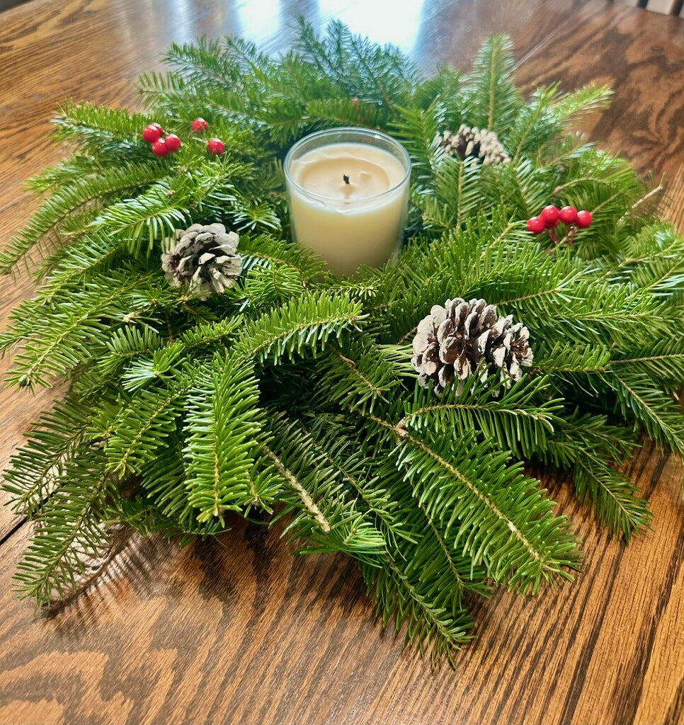 Decorative center piece with a candle, pine cones, and berries on a wooden surface